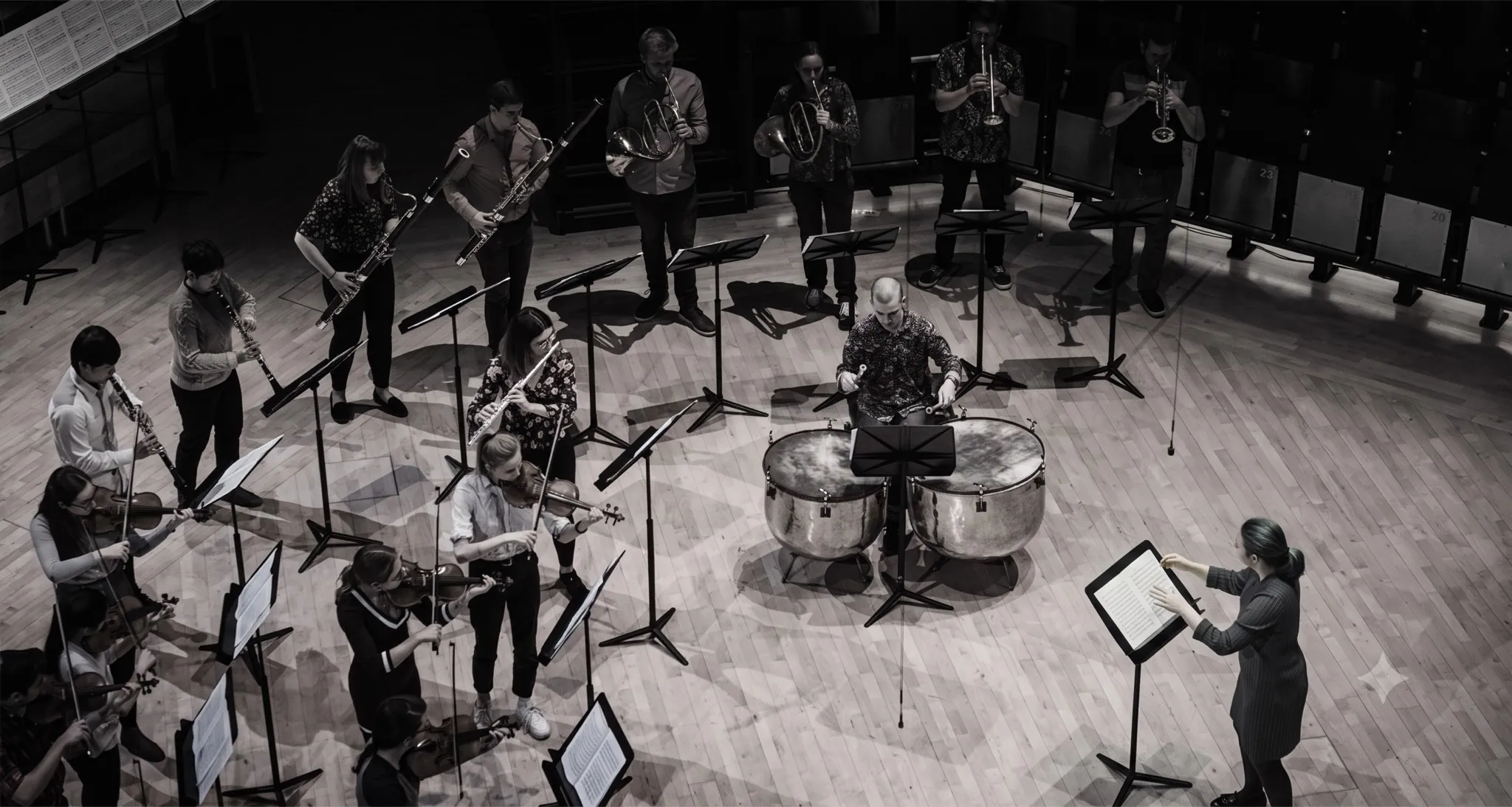 An orchestra rehearsing on a wooden stage, every musician following the conductor at the podium